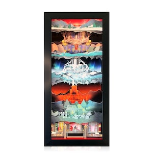 May include: A framed paper art piece depicting a multi-layered landscape with a castle, waterfall, and mountains. The artwork is framed in black and has a red, white, and blue color scheme.