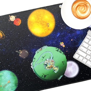 May include: A black desk mat featuring a colorful outer space design with planets, stars, and a bright yellow sun. A white keyboard and a cup of coffee with latte art are on the mat.