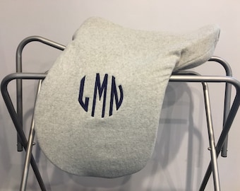 May include: Grey fleece saddle pad with a navy blue monogram of the letters LMN in a circle.