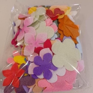 May include: A clear plastic bag filled with assorted felt flower shapes in various colors. The flowers include shades of pink, red, yellow, orange, purple, and white. These craft supplies are ideal for DIY projects and decorations.
