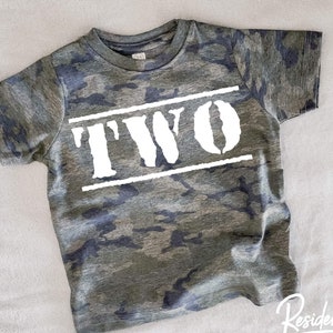 May include: Camouflage green t-shirt with white text that says "TWO" in a bold, blocky font.