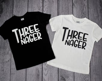 May include: Two black and white t-shirts with the text "Three Nager" printed on them.