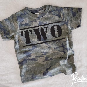 May include: Camouflage green t-shirt with black text that says "TWO" in a bold, blocky font.