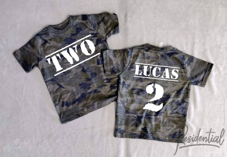 May include: Two camouflage t-shirts with white text. One shirt says "TWO" and the other says "LUCAS 2".