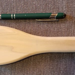 May include: A wooden spatula with a rounded handle and a flat, slightly curved blade. The spatula is made of light-colored wood and is about 10 inches long.