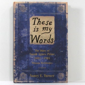 Può includere: Una copertina di libro blu con il titolo "These is my Words" in lettere corsive nere. Il libro è un romanzo intitolato "The Diary of Sarah Agnes Prine, 1881-1991 Arizona Territories" di Nancy E. Turner.