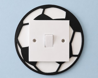 May include: A white light switch with a black soccer ball design around it. The soccer ball design is a black outline of the ball's panels. The light switch is mounted on a light blue wall.