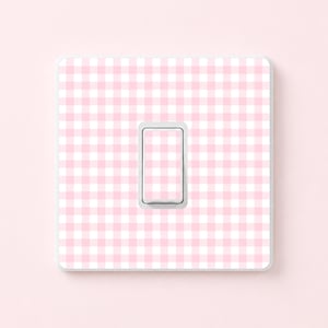 May include: A light pink and white gingham pattern light switch cover. The switch plate has a rectangular shape with a single rocker switch in the center. The background is a solid light pink.