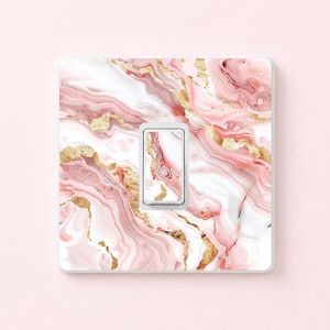 Puede incluir: Una cubierta decorativa para interruptor de luz con un interruptor basculante único. La cubierta presenta un diseño de mármol rosa, blanco y dorado. La placa del interruptor tiene un borde blanco y un patrón de mármol a juego en el interruptor basculante.