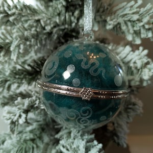 May include: A teal blue glass Christmas ornament with a silver metal hinged lid. The ornament is decorated with white polka dots and a silver snake design.
