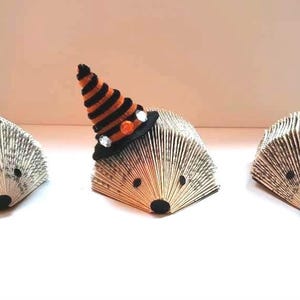 Pode incluir: Tr&ecirc;s ornamentos de ouri&ccedil;o feitos com p&aacute;ginas de livros decorados para o Halloween. Um tem um chap&eacute;u de bruxa, outro tem um milho doce e outro tem um la&ccedil;o.
