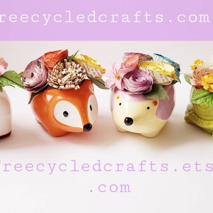 May include: Four small ceramic planters in the shapes of a unicorn, fox, hedgehog, and turtle, each with a colorful paper flower arrangement. The planters are arranged in a row on a white surface. The text "Treecycledcrafts.com" is visible at the top of the image, and the text "Treecycledcrafts.etsy.com" is visible at the bottom of the image.