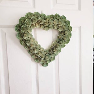 May include: A green paper heart wreath with a white background. The wreath is made of many small paper rosettes.