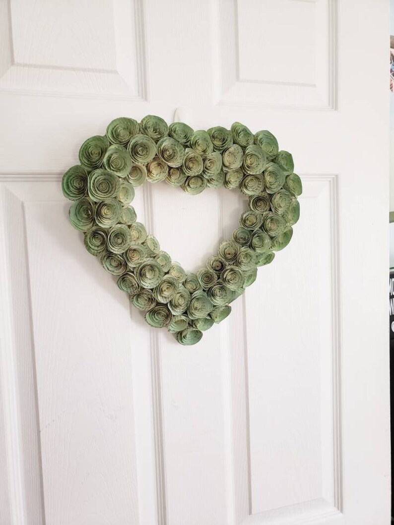 May include: A green paper heart wreath with a white background. The wreath is made of many small paper rosettes.