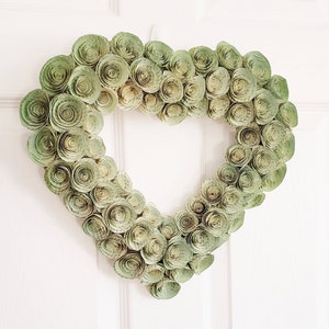 May include: A heart-shaped wreath made of paper rosettes in shades of green. The rosettes are arranged in a spiral pattern, creating a textured and dimensional effect.