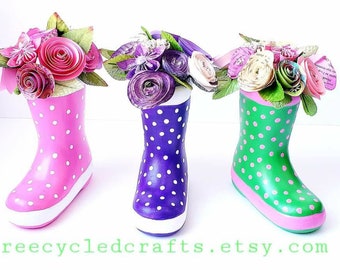 May include: Three rain boots painted in pink, purple, and green with white polka dots. Each boot is filled with a bouquet of paper flowers.