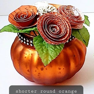 May include: A short, round, orange mercury glass pumpkin with a decorative arrangement of paper flowers. The flowers are made of brown paper and have a vintage look.