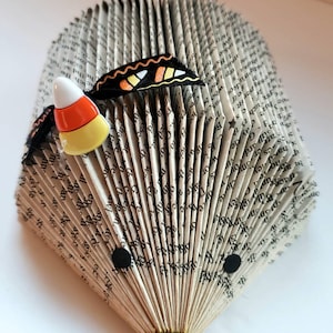 Pode incluir: Um livro dobrado na forma de um ouri&ccedil;o com uma borboleta preta e laranja e uma decora&ccedil;&atilde;o de milho doce no topo.