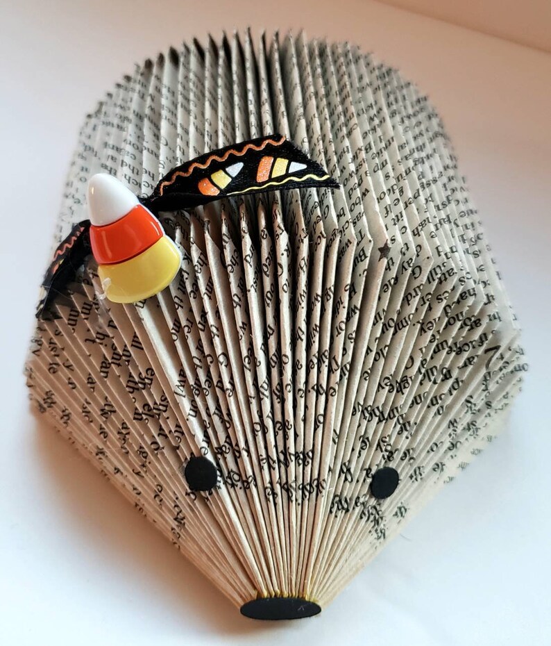 Pode incluir: Um livro dobrado na forma de um ouri&ccedil;o com uma borboleta preta e laranja e uma decora&ccedil;&atilde;o de milho doce no topo.