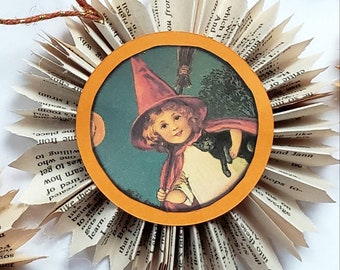 May include: A witch with a black cat on her shoulder is featured in a round, orange-framed picture. The picture is attached to a paper starburst made from pages of a book. The starburst is decorated with a brown twine string.