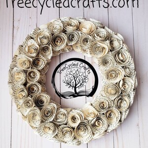 K&ouml;nnte beinhalten: Ein kreisf&ouml;rmiger Kranz aus gerollten Papierrosen, mit dem Text "Treecycledcrafts.com" oben. In der Mitte des Kranzes befindet sich ein kreisf&ouml;rmiges Logo mit einem Baumdesign. Die Rosen sind in verschiedenen Creme- und Beiget&ouml;nen gehalten.