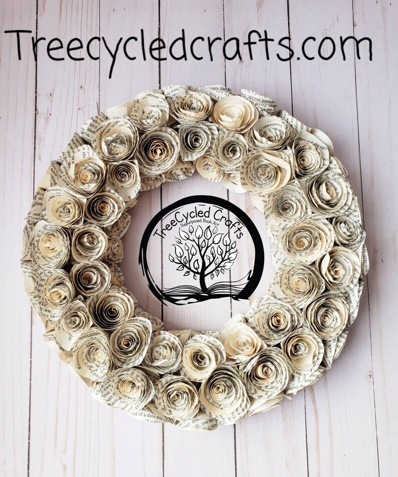 K&ouml;nnte beinhalten: Ein kreisf&ouml;rmiger Kranz aus gerollten Papierrosen, mit dem Text "Treecycledcrafts.com" oben. In der Mitte des Kranzes befindet sich ein kreisf&ouml;rmiges Logo mit einem Baumdesign. Die Rosen sind in verschiedenen Creme- und Beiget&ouml;nen gehalten.