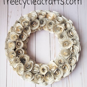 K&ouml;nnte beinhalten: Ein kreisf&ouml;rmiger Kranz aus gerollten Papierrosen, der verschiedene Creme- und Beiget&ouml;ne aufweist. Die Rosen bestehen aus Buchseiten und erzeugen eine einzigartige Textur. Der Text "treecycledcrafts.com" ist oben sichtbar.