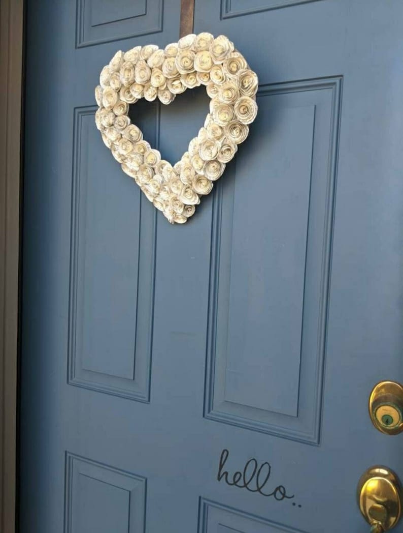 May include: A blue door with a white paper heart wreath hanging on it. The wreath is made of paper rosettes. The door has a gold door knocker and the words "hello..." written on it.