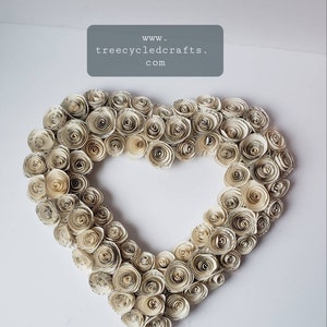 May include: A heart-shaped wreath made of paper roses, each rose is made from recycled book pages. The wreath is white with a slight cream color. The text "www.treecycledcrafts.com" is visible in the top center of the image.