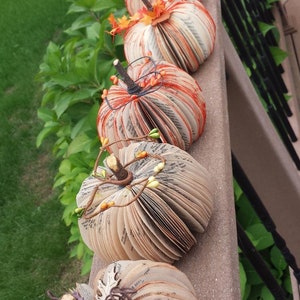 Pumpkins s made from book pages, various embellishments such a pine cones,  berries or twine.  The pumpkins stem is made from a twig branch. Colors available are natural book color and orange,