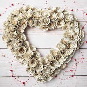 May include: A heart-shaped wreath made of paper roses, each rose is made from pages of a book. The wreath is decorated with a string of red and white beads.