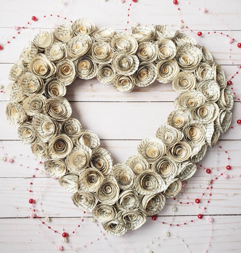 May include: A heart-shaped wreath made of paper roses, each rose is made from pages of a book. The wreath is decorated with a string of red and white beads.