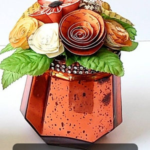 May include: Tall geometric orange mercury glass pumpkin vase with a bouquet of paper flowers. The flowers are made from book pages and are in shades of orange, yellow, and white.