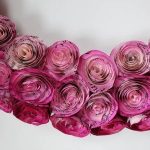 May include: A pink paper flower wreath made from pages of a book. The flowers are arranged in a circle and have a delicate, romantic look.
