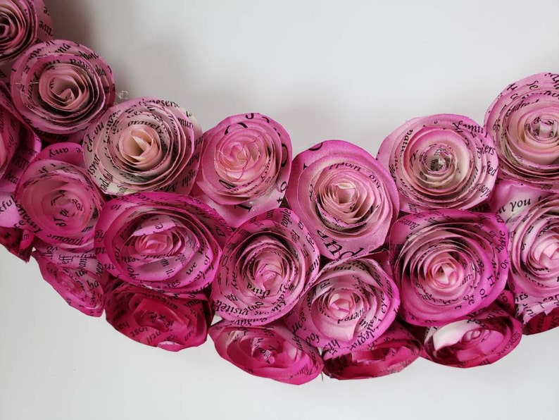 May include: A pink paper flower wreath made from pages of a book. The flowers are arranged in a circle and have a delicate, romantic look.