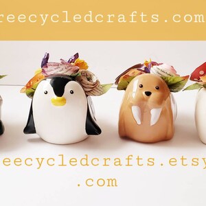 May include: Four ceramic animal figurines with floral crowns made of paper. The animals are a moose, penguin, walrus, and polar bear. The flowers are in shades of pink, purple, orange, and yellow. The figurines are on a white surface. Treecycledcrafts.com and Treecycledcrafts.etsy.com are written below the figurines.
