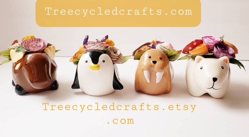 May include: Four ceramic animal figurines with floral crowns made of paper. The animals are a moose, penguin, walrus, and polar bear. The flowers are in shades of pink, purple, orange, and yellow. The figurines are on a white surface. Treecycledcrafts.com and Treecycledcrafts.etsy.com are written below the figurines.