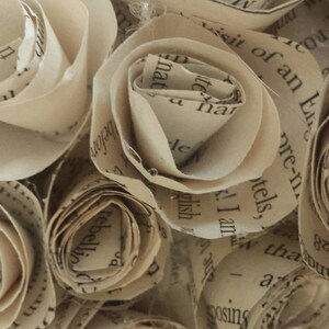 K&ouml;nnte beinhalten: Nahaufnahme von Papierrosen, jede sorgf&auml;ltig aus Buchseiten gefertigt. Die Rosen befinden sich in verschiedenen Bl&uuml;hstadien und zeigen die zarte Textur und den gedruckten Text. Die Farbe ist ein warmes, gealtertes Beige.