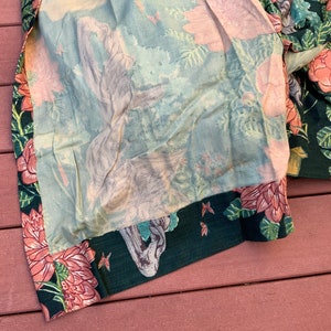 May include: A green fabric with a floral pattern featuring pink flowers and green leaves. The fabric has a light blue lining with a faded floral pattern.