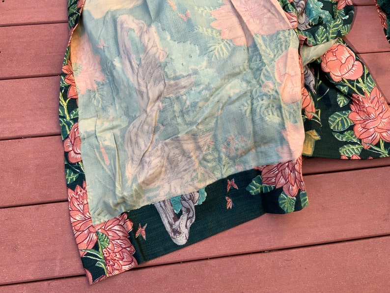 May include: A green fabric with a floral pattern featuring pink flowers and green leaves. The fabric has a light blue lining with a faded floral pattern.