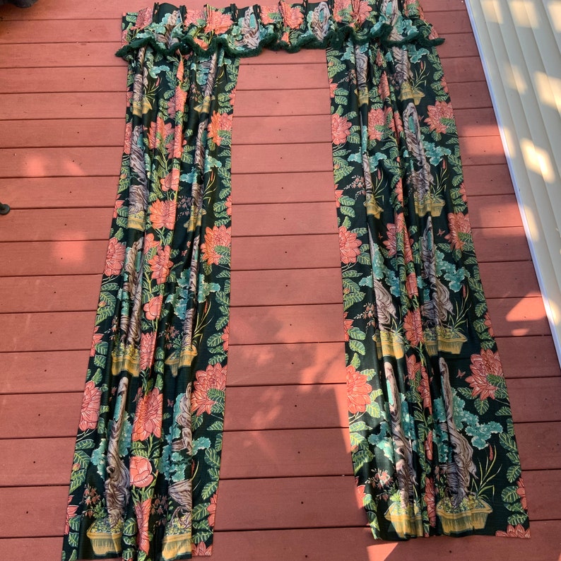 May include: A pair of green and pink floral curtains with a ruffled top. The curtains are hanging on a wooden deck.