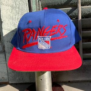 May include: A blue and red baseball cap with the words "New York Rangers" and a logo of the team on the front.
