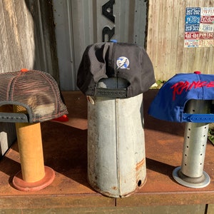 May include: Three baseball caps displayed on stands. The cap on the left is black with a red mesh back and a black brim. The middle cap is black with a blue lightning bolt logo. The cap on the right is blue with a red "RANGERS" logo.