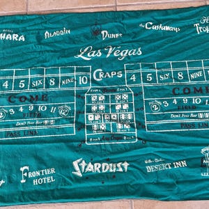 May include: Green craps table cloth with white markings and text. Features the words "Las Vegas" and various casino names like "Sahara" and "Stardust". Includes dice combinations and betting areas.