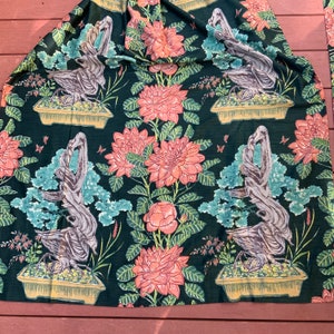 May include: A dark green fabric with a repeating pattern of stylized bonsai trees and pink flowers. The trees are brown and have a textured look. The flowers are a light pink with a yellow center.