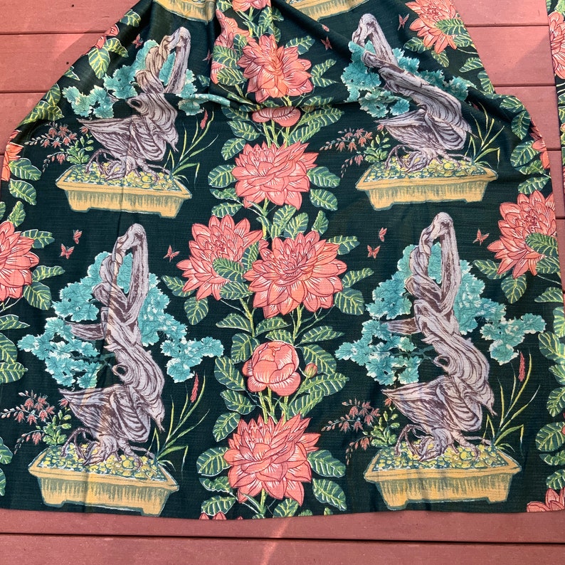 May include: A dark green fabric with a repeating pattern of stylized bonsai trees and pink flowers. The trees are brown and have a textured look. The flowers are a light pink with a yellow center.