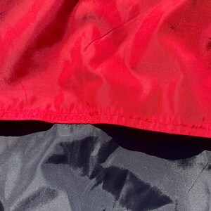 Puede incluir: Primer plano de tela roja y azul marino. La tela roja est&aacute; en la parte superior, con una costura visible. La tela azul marino est&aacute; debajo. Las telas tienen un aspecto brillante y ligeramente arrugado.