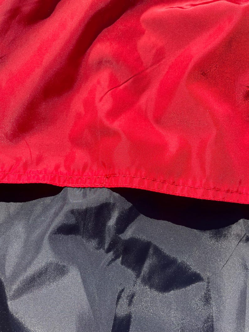 Puede incluir: Primer plano de tela roja y azul marino. La tela roja est&aacute; en la parte superior, con una costura visible. La tela azul marino est&aacute; debajo. Las telas tienen un aspecto brillante y ligeramente arrugado.