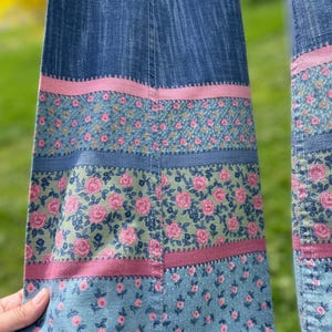 Pu&ograve; includere: Primo piano di tessuto denim con accenti floreali. Il denim blu presenta strisce rosa e floreali. Il motivo floreale comprende rose rosa su sfondo verde. Il design &egrave; un mix di stili vintage e moderni.