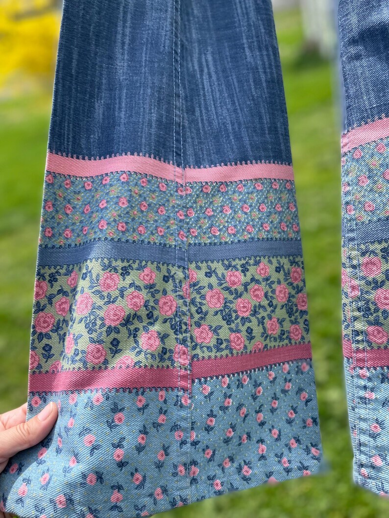 Pu&ograve; includere: Primo piano di tessuto denim con accenti floreali. Il denim blu presenta strisce rosa e floreali. Il motivo floreale comprende rose rosa su sfondo verde. Il design &egrave; un mix di stili vintage e moderni.